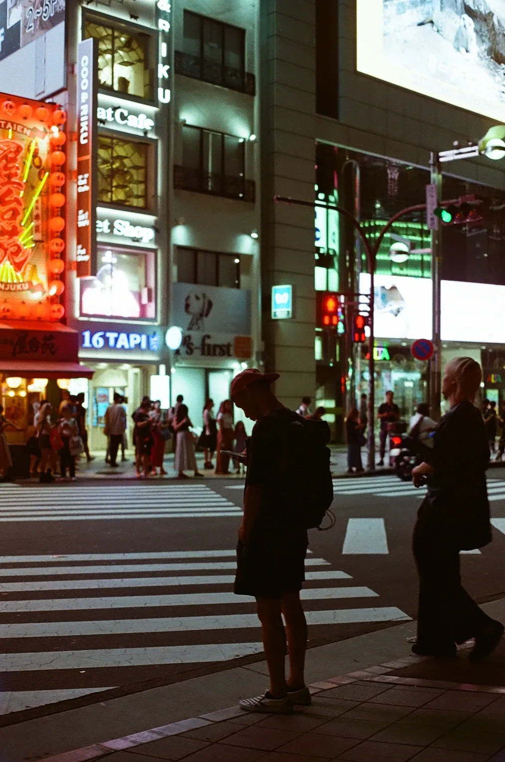 A man staring at his phone screen by a crossing in Shinjuku, at night.