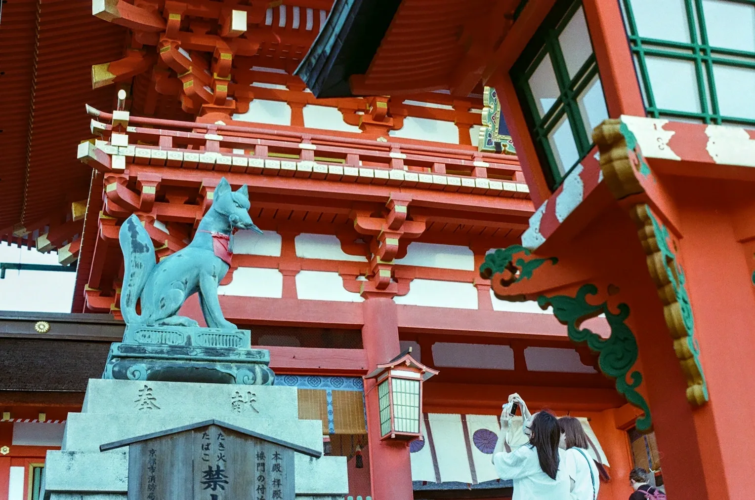 Two girls taking pictures of a kitsune statue in Fushimi Inari shrine.